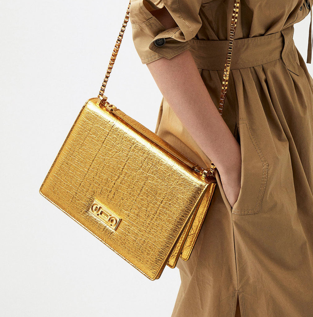 The Cristiana Vegan Shoulder Bag carried by a model in gold Piñatex, featuring 24K gold-plated hardware and sculptural proportions designed for contemporary elegance.