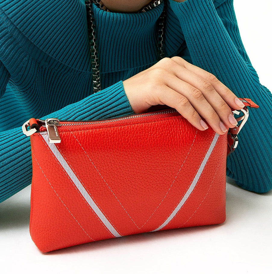 Detail of a model carrying The Arianna Monochrome Pouch in Coral grained leather, highlighting sculptural V-shaped detailing and contemporary Italian craftsmanship.