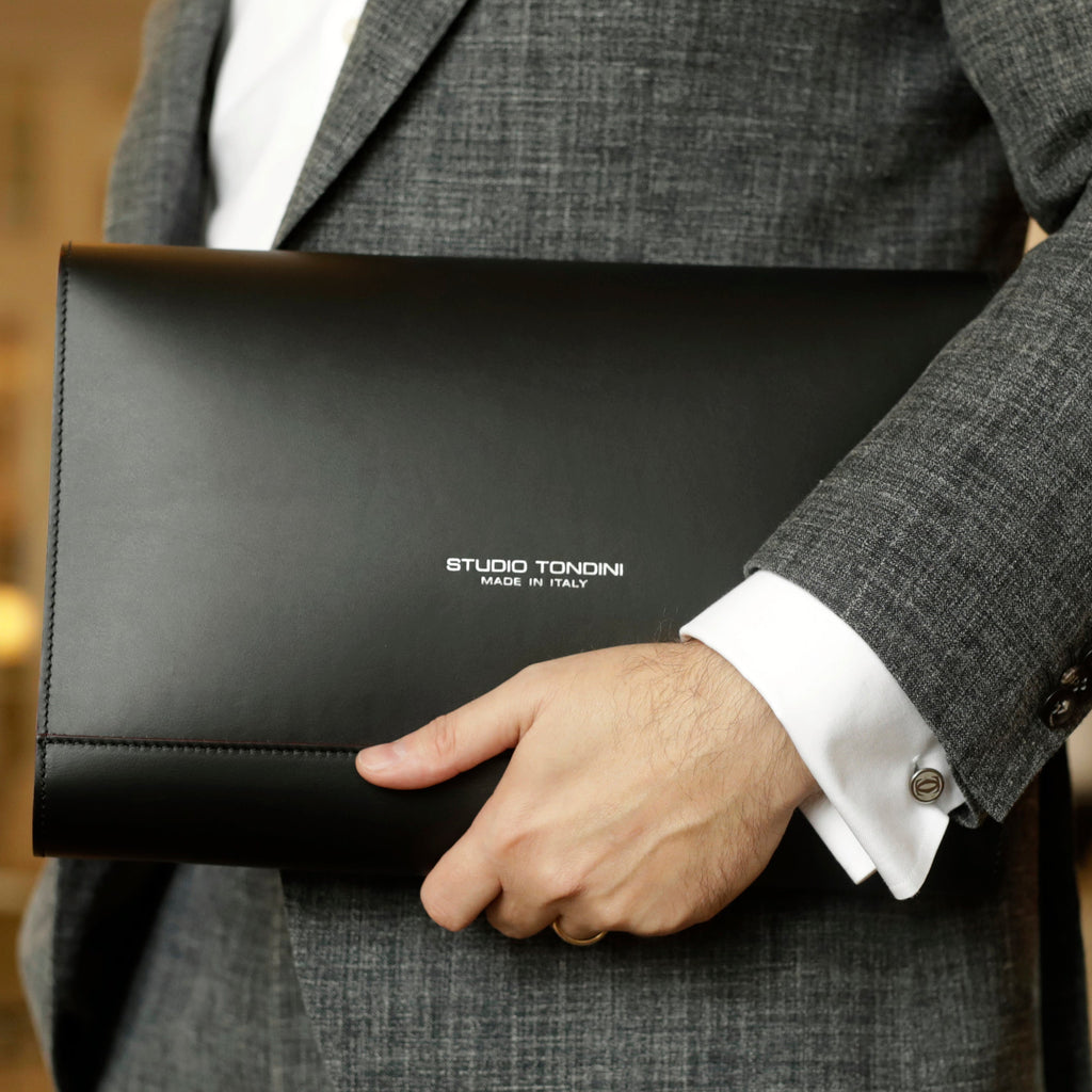 Model carrying The Document Holder in smooth black leather with bordeaux edge detailing, expressing refined professionalism and contemporary sophistication.