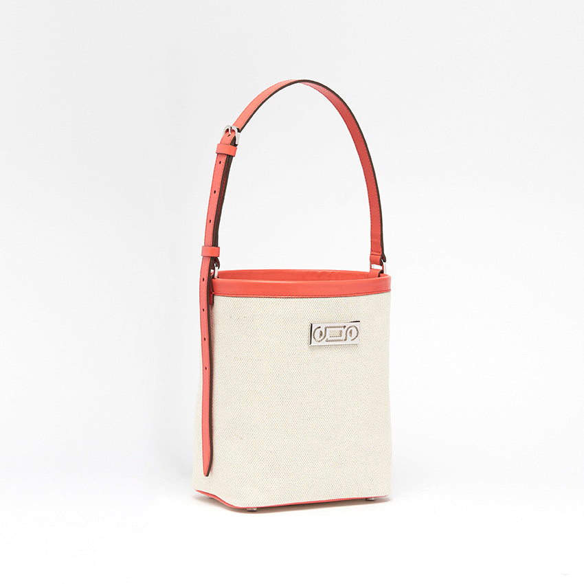 The Francesca Canvas Bucket Bag. Three-quarter view showing natural canvas with coral calf leather detailing and adjustable strap for short or long styling.