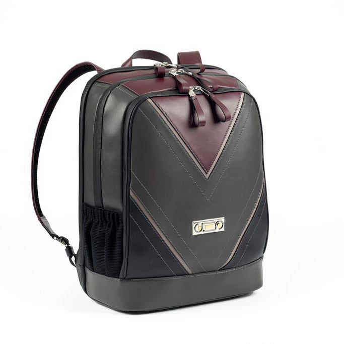 Three-quarter view of The Simona Backpack with Studio Tondini’s signature V-shape construction creating a bordeaux leather triangle, showcasing architectural contemporary craftsmanship.